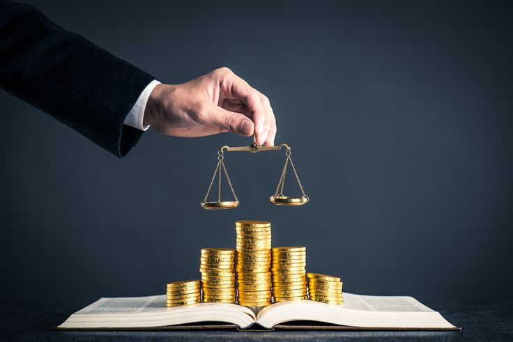 دستی که ترازو در دست دارد و روی میز سکه و اسکناس برای نشان دادن تعادل سیاست پولی انبساطی و انقباضی